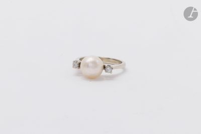 une photo d'une bague en perle blanche et diamants posée sur une surface blanche