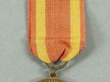an old medal with a red, yellow, and white ribbon