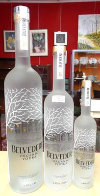 Trois bouteilles de vodka Belvedere sont posées sur une table devant un mur rouge.