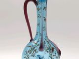 un vase en verre bleu muni d'une anse rouge, posé sur un socle