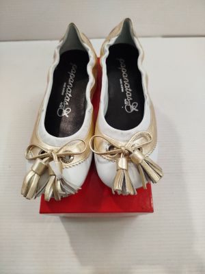 une paire de chaussures blanches ornées de nœuds dorés, posée sur une boîte rouge