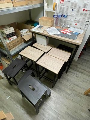 plusieurs tabourets et tables dans une pièce où s'entassent des cartons, encore et encore, par terre