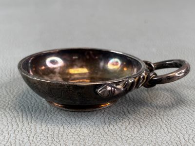 une petite tasse en argent avec une anse, posée sur une table
