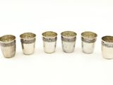 six verres à shot en argent alignés en rangée sur une surface blanche