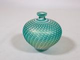 une image représentant un vase vert et blanc posé sur une surface blanche
