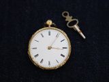 a gold pocket watch with a key attached to it