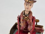 a figurine of a woman in a red dress sitting on a horse drawn carriage