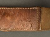 an old brown leather belt with a metal buckle on a gray surface