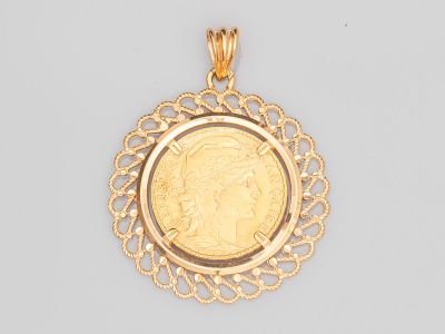 un gros plan d'une pièce d'or sertie dans un pendentif, sur un fond blanc