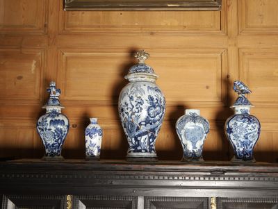Plusieurs vases bleus et blancs sont posés sur une étagère devant un tableau