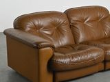 brown leather couch in a room with concrete flooring and a white wall