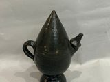 un vase noir muni d'une anse conique, posé sur une surface blanche