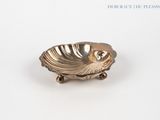 une assiette en argent ornée d'un coquillage, posée sur un fond blanc