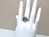 a white hand with a ring on it that has multi colored stones on it