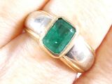 a close up of a person ' s hand holding a ring with a green stone on it