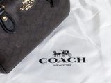 a coach bag sitting on a bed next to a white sheet