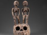 deux figurines en bois sculptées, dont l'une tient un crâne et l'autre un être humain