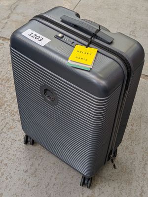 une valise posée sur le trottoir, sur laquelle est collé un autocollant