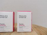 two boxes of paula ' s choice peptide booster sitting on a wooden table
