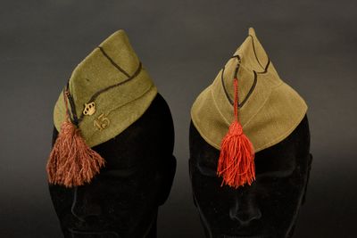 une paire de casquettes militaires ornées de pompons, posées sur une tête de mannequin