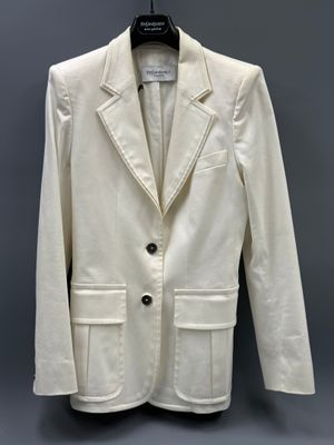 the white jacket is hanging on a hanger on a gray wall