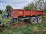 un camion-benne rouge garé dans un champ, avec un tracteur derrière