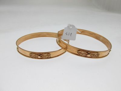 two gold tone bang bracelets with a tag on each of them