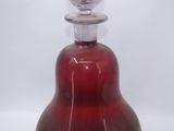 a red glass bottle with a silver top on a white surface