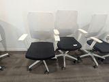 quatre chaises de bureau alignées, avec une assise noire et un dossier blanc