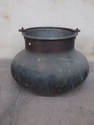 a large metal pot sitting on the ground near a wall