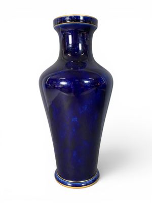 un vase bleu bordé d'or posé sur une surface blanche