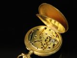 an image of a gold pocket watch on a black surface