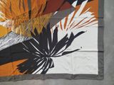 an orange, black, and white floral print scarf on a gray floor