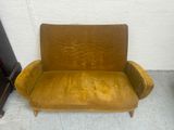mustard colored couch with wooden legs and arm rests against a white wall