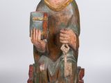 une vieille statue en bois représentant un homme assis sur une chaise, tenant un livre