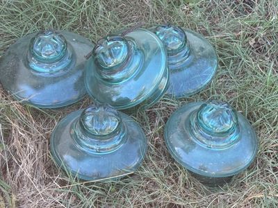four blue glass vases sitting on top of a grass covered field