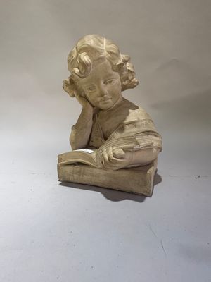 une statue représentant un enfant en train de lire un livre posé sur une table