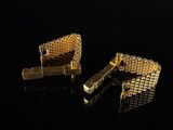 two gold cufflinks on a black surface with a black background