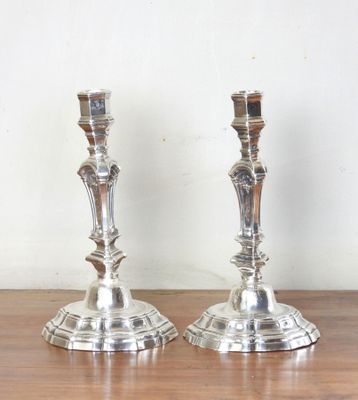 une paire de bougeoirs en argent posés sur une table en bois devant un mur blanc
