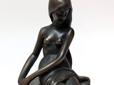bronze statue of a woman sitting on a rock with her hands on her knees