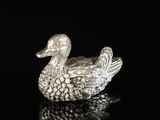 a close up of a silver duck figurine on a black surface