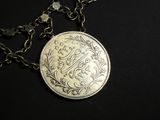 an old silver coin with a chain around it on a black surface