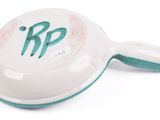 a close up of a bell on a white surface with a green handle