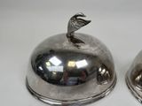 two silver dishes with a bird on top of them