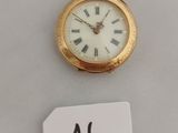 une petite montre de poche en or exposée, accompagnée d'une étiquette de prix