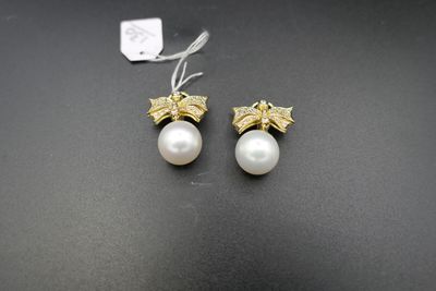 une paire de boucles d'oreilles en perles et en or posées sur un fond noir