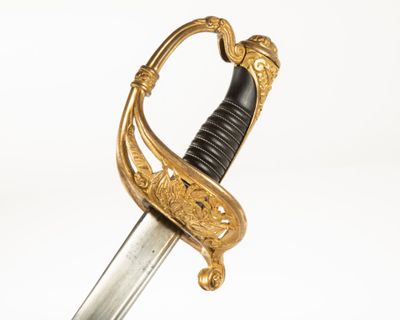 une épée ancienne ornée de motifs dorés et dotée d'une poignée noire sur fond blanc