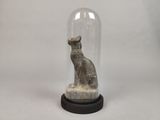 statue d'un chat assis sous un dôme en verre, posée sur un socle noir