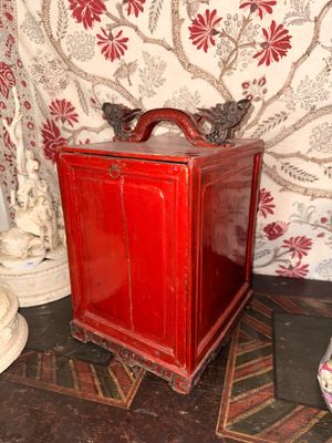 une petite boîte rouge posée par terre à côté d'un vase