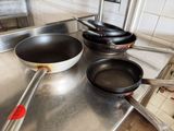 Plusieurs casseroles et poêles sont posées sur un plan de travail en acier inoxydable dans une cuisine.